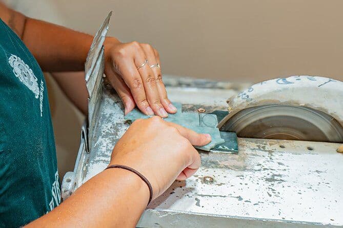 Hands shaping a piece of green jade against a cutting wheel in a jade workshop