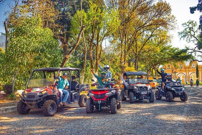 Guests waving from off-road buggies and ATVs on a cobblestone street lined with trees
