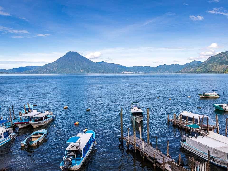Boats moored at wooden docks on Lake Atitlán, with a volcano across the water